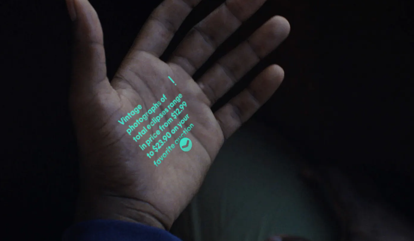 Projected text from an AI device onto a person's palm reading 'Vintage photographs of [...] total clips range in price from $1.99 to $23.90 on your favorite action' with a green heart emoji."